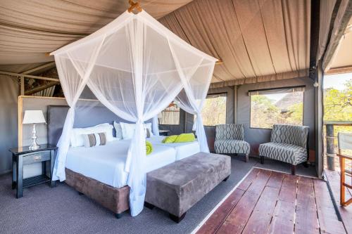 1 Schlafzimmer mit einem Himmelbett und 2 Stühlen in der Unterkunft Eagle Tented Lodge & Spa in Okaukuejo