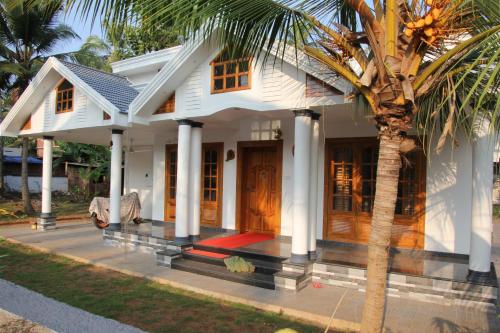 a white house with a palm tree in front of it at Belhaven Home Stay in Trivandrum