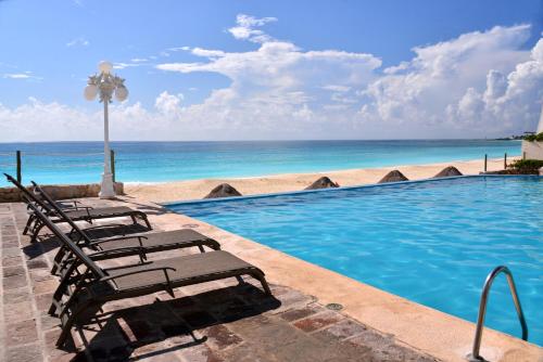 a swimming pool with two lounge chairs and the ocean at BSEA Cancun Plaza Hotel in Cancún