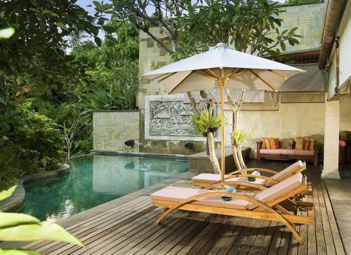 a chair with an umbrella next to a swimming pool at Gending Kedis Luxury Villas & Spa Estate in Jimbaran