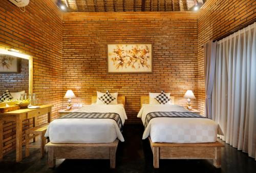 two beds in a room with a brick wall at De Umah Bali Eco Tradi Home in Bangli