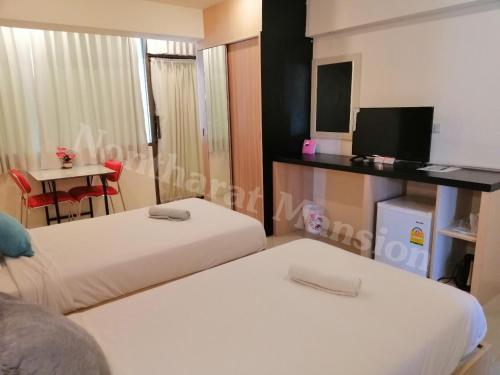 a room with two beds and a table with a television at Nontharat Mansion in Nonthaburi