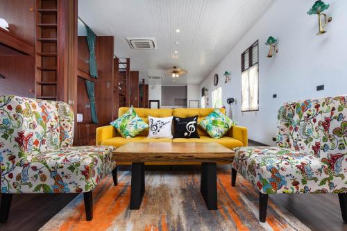 a living room with a yellow couch and two chairs at Sound Gallery House - SHA Plus in Phuket Town