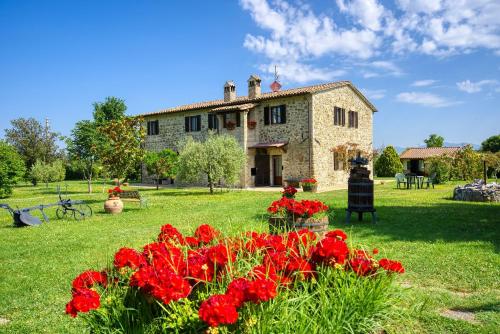 ein großes Steinhaus mit roten Blumen im Hof in der Unterkunft Agriturismo Le Terre del Casale in Assisi