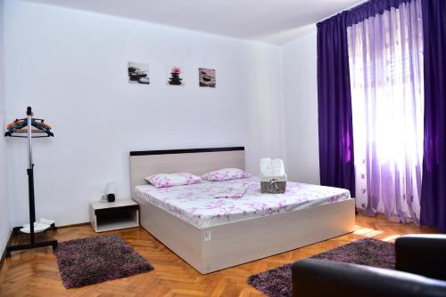 a white bedroom with a bed with purple curtains at Vila Arjana in Orşova