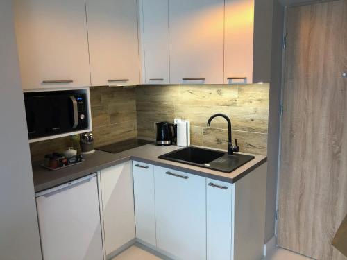 een keuken met witte kasten, een wastafel en een magnetron bij CR Wygodny Apartament w Centrum Nowy Świat 13 in Białystok