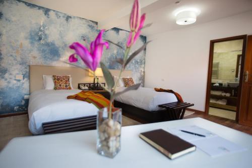 a room with two beds and a vase with flowers on a table at Tocuyeros Boutique Hotel in Cusco