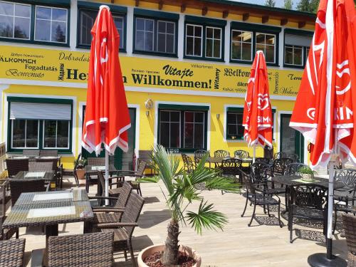 a restaurant with tables and chairs and red umbrellas at Gasthof Klug zum Ehrensepp in Modriach