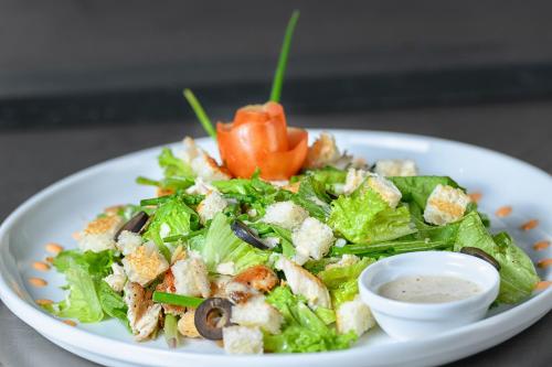a salad on a white plate with a bowl of dressing at Aryana Boutique Hotel in Anuradhapura