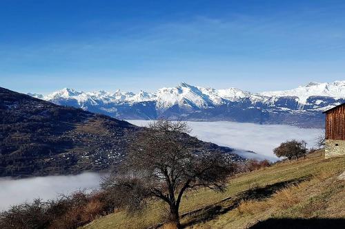 a barn on a hill with snow covered mountains at La Chaumière d'Hérens in Vernamiège