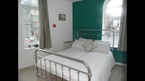 a bed in a bedroom with a green wall and two windows at 1 Tŷ Mona Church Street Apartment in Llangefni