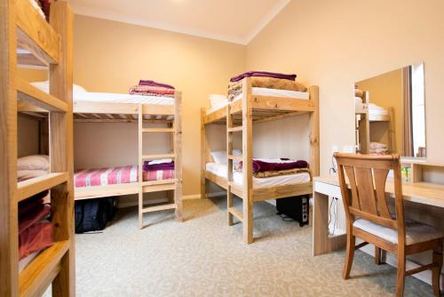 a room with bunk beds and a desk and a chair at The Prince Albert Backpackers & Bar in Nelson
