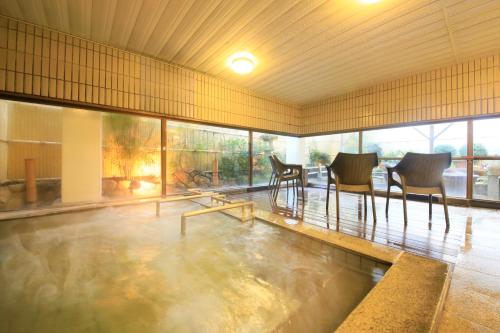 a room with a pool of water with chairs and tables at Hotel Kamogawaso in Takekara