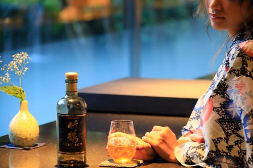 a woman sitting at a table with a bottle and a glass at Hotel Kamogawaso in Takekara