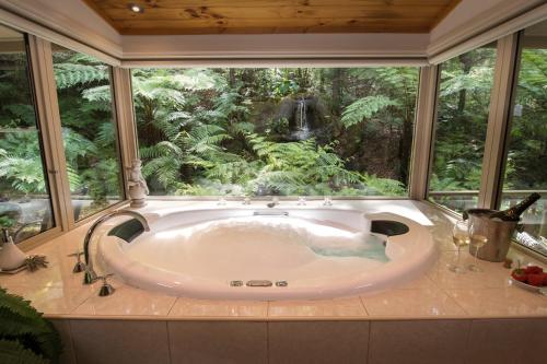 bañera en una habitación con ventana grande en Myers Creek Cascades Luxury Cottages, en Healesville