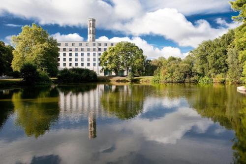 a building with a reflection in a lake at Steigenberger Parkhotel Braunschweig in Braunschweig