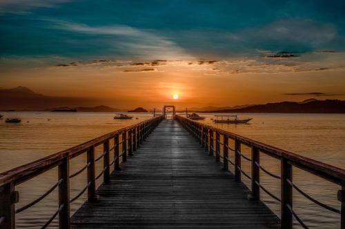 un muelle de madera con la puesta de sol en el fondo en Kokomo Resort Gili Gede, en Gili Gede
