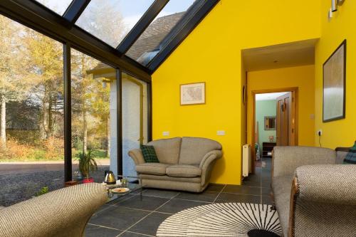 a conservatory with a yellow wall and two chairs at Powdermills B & B in Inveraray