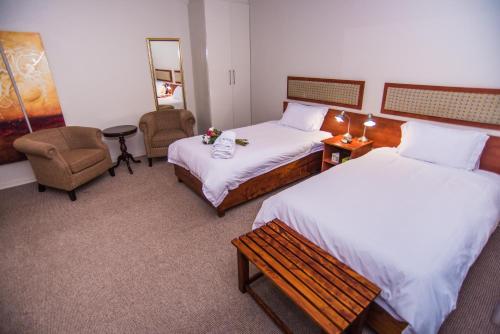 a hotel room with two beds and a chair at Adelante Lodge in Bloemfontein