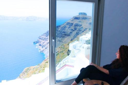 a woman sitting in a window looking out at the ocean at Smaro Studios in Firostefani