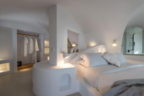 a white bedroom with a white bed and a mirror at Nefeles Luxury Suites in Fira