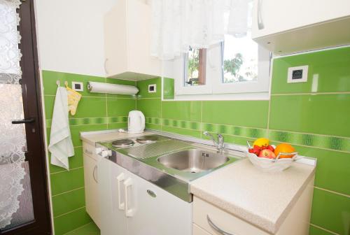 a green kitchen with a sink and a bowl of fruit at Apartment Zvone in Baška
