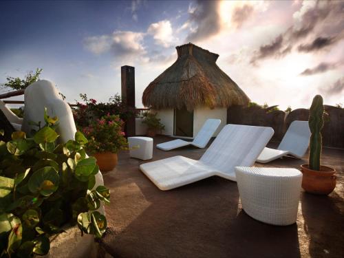 a patio with white chairs and a thatch hut at Kinbe Hotel Boutique in Playa del Carmen