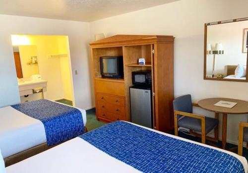 a hotel room with two beds and a desk and a table at Travelodge by Wyndham Cedar City in Cedar City