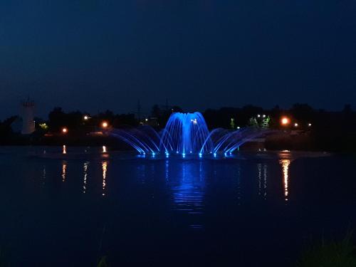a fountain in the middle of a pond at night at SaMuci Apartman in Hajdúszoboszló