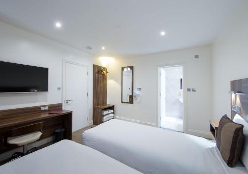 a hotel room with two beds and a flat screen tv at Heathrow-Windsor Guest House in Slough