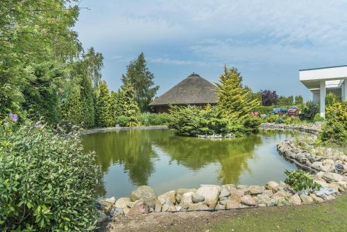 a pond in a garden with a building in the background at Nowa Dana Ośrodek Wypoczynkowy in Łebcz