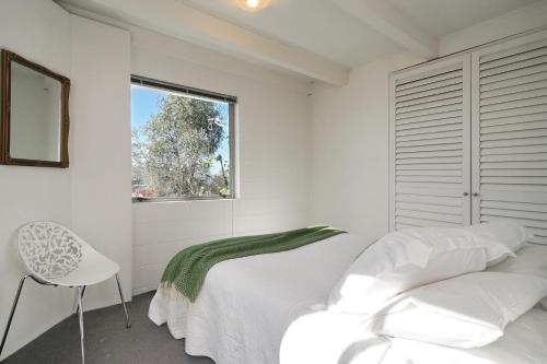 a white bedroom with a bed and a window at Retro Living - Lush Garden in Christchurch
