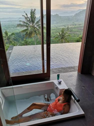 a woman laying in a bath tub with a view at Villa di Bias in Tirtagangga