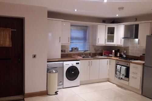 a kitchen with white cabinets and a washer and dryer at Cosy Castlerock Beside Beach Golf Course and Pub in Castlerock