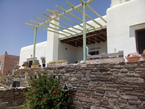 a stone wall in front of a white building with a pergola at Cycladic House in Vari