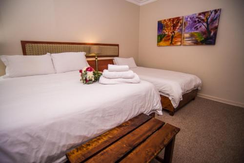 two beds in a room with white sheets and flowers at Adelante Lodge in Bloemfontein