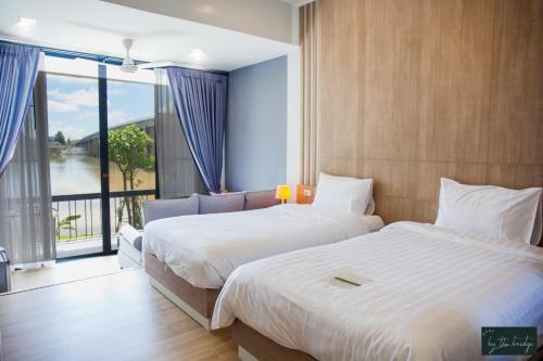 two beds in a hotel room with a large window at Home by the Bridge Hotel in Kamphaeng Phet