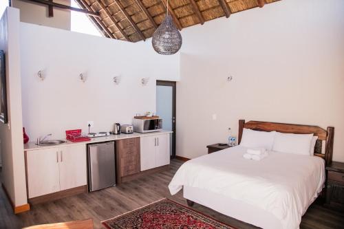 a bedroom with a white bed and a kitchen at Kuwisa Lodge in Bela-Bela
