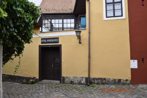 a yellow building with a black door and a window at Főtér Apartmanház Szentendre in Szentendre