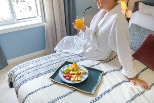 a woman sitting on a bed with a plate of fruit and a drink at La Villa Boutique Hotel in Budva