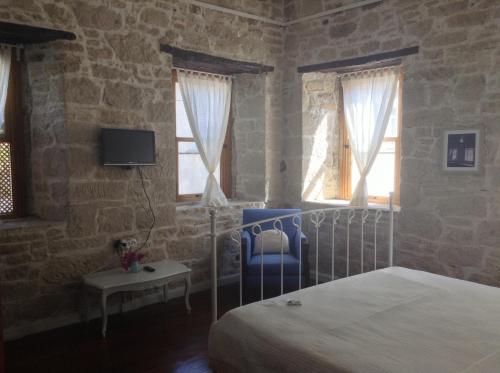a bedroom with a bed and a chair and windows at Eski Tas Hotel in Cesme
