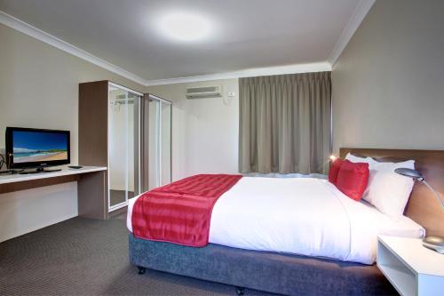a hotel room with a large bed and a television at Quality Hotel City Centre in Coffs Harbour