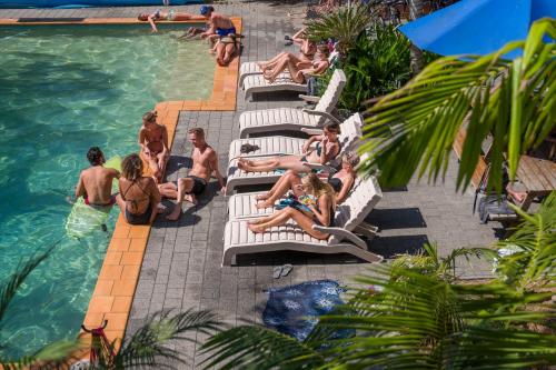 a group of people sitting on lounge chairs by a swimming pool at YHA Cape Byron, Byron Bay in Byron Bay