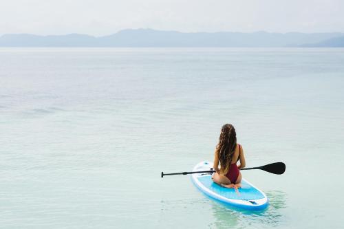 una mujer sentada en una tabla de surf de remo en el agua en The Seraya Resort Komodo, en Labuan Bajo