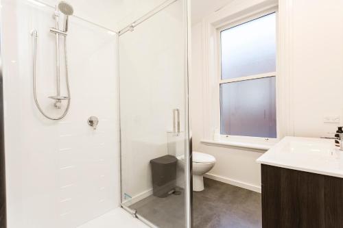 a white bathroom with a shower and a toilet at The Stuart Street Terraced House in Dunedin