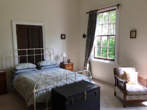 um quarto com uma cama, uma cadeira e uma janela em The Old School House em Te Awamutu