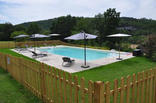 a pool with chairs and umbrellas and a fence at gîtes les 7 roches 6 couchages in Les Eyzies-de-Tayac