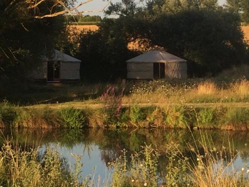 an old yurt in a field next to a body of water at Holiday home on farm (La Ferme du Tao) in Beaugies-sous-Bois