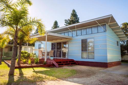 une maison bleue avec un palmier en face dans l'établissement Barlings Beach Holiday Park, à Tomakin