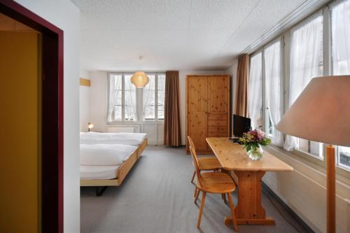 a room with a bed and a table and a bed and windows at Hotel Krone Budget in Lenk
